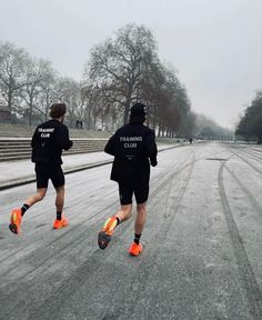 two men in black jackets and orange shoes running down the street on snow covered ground