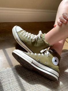 a person's legs and feet with green converses on them, sitting on the floor