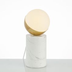 a white and gold table lamp on top of a marble base with a round light bulb