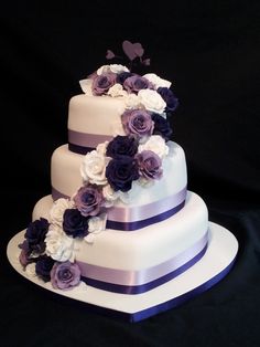 a three tiered wedding cake with purple and white flowers on the top, in front of a black background