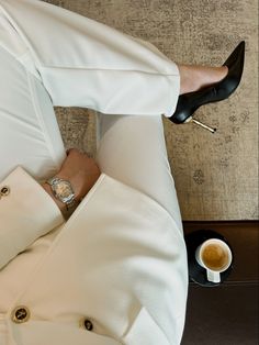 a man in white suit and black shoes sitting on a couch with his legs crossed