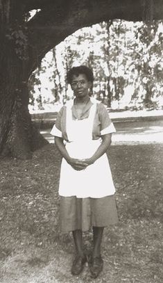 an old black and white photo of a woman standing in front of a large tree