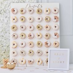 a white table topped with lots of donuts next to a sign and some flowers