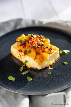 a black plate topped with food on top of a white table cloth and napkins