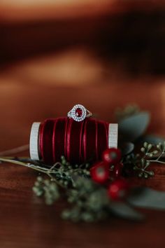 an engagement ring sitting on top of a red ribbon next to berries and greenery