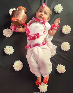 a baby dressed in pink and white laying on a black surface with flowers around her