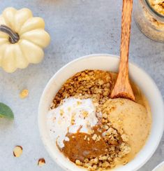 a bowl filled with oatmeal next to two pumpkins and a wooden spoon