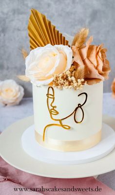 a white cake with gold decoration and flowers on the top is sitting on a plate