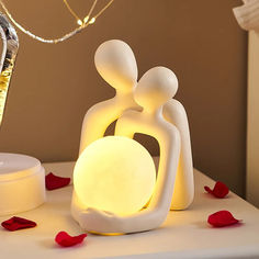 a white table topped with a lamp next to a vase filled with red rose petals