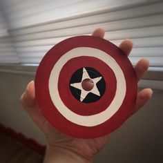 a hand holding a red and white shield with a star painted on the center, in front of a window