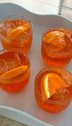 four glasses filled with orange juice on top of a white tray