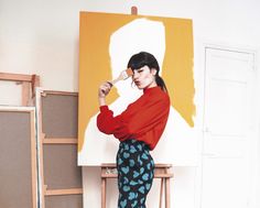 a woman is standing in front of a painting and posing for the camera with her hands on her hips