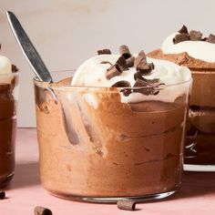 two desserts with ice cream, chocolate chips and whipped cream in glass dishes on a pink surface