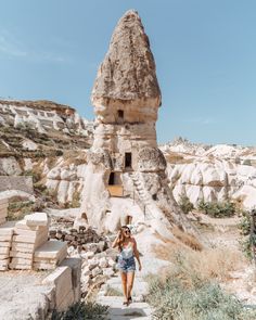 a woman is walking up some steps in front of a rock formation with a house built into it