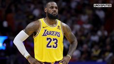 a man with a beard standing in front of a crowd wearing a lakers jersey and holding his hands on his hips