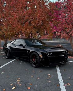 a black sports car parked in a parking lot next to some trees with red leaves