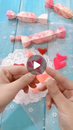 two hands are making hearts out of paper on a blue table with white doily