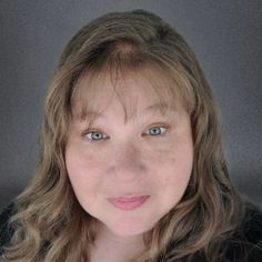 a woman with long hair and blue eyes looking at the camera while wearing a black shirt