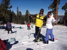 two people standing on skis in the snow with other skiers and snowboarders behind them