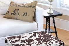 a cow print ottoman sits in front of a white couch with a brown and white pillow