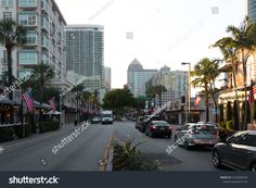 cars driving down the street in front of tall buildings and palm trees on either side