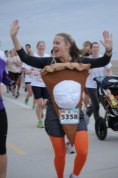 a group of people that are running in a race with their arms up and one person wearing an animal costume