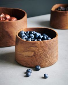 two wooden bowls filled with blueberries sitting on top of a white counter next to some silver balls