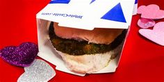 a hamburger in a paper box with hearts around it on a red table top,