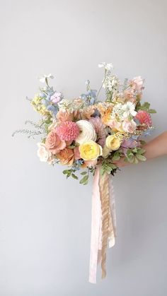 a bridal bouquet being held by someone's hand against a gray wall with white and pink flowers