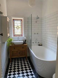 a white bath tub sitting next to a sink in a bathroom with black and white tiles