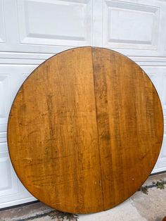 a round wooden table sitting in front of a white garage door on the side of a building