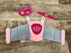 a pink and gray belt with two pairs of scissors next to it on a wooden floor