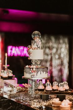 a three tiered cake sitting on top of a table next to cupcakes