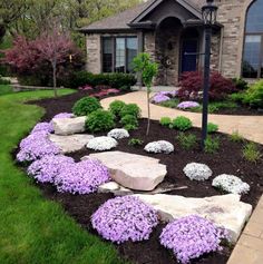 landscaping in front of a house with purple flowers and rocks on the ground, near a lamp post