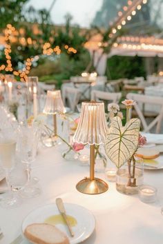 the table is set with white plates and silverware, gold candlesticks and glass vases