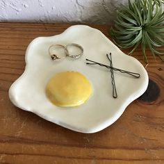 an egg and two wedding rings are on a white plate next to a succulent plant