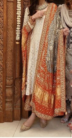 two women standing next to each other in front of a wooden door wearing dresses and scarves