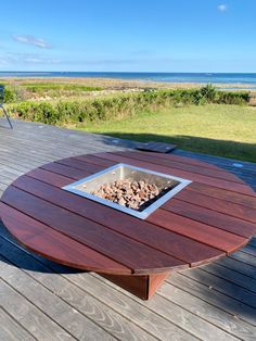 an outdoor fire pit sitting on top of a wooden deck next to the ocean and grass