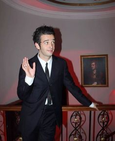 a man in a suit and tie standing next to a railing with his hands up