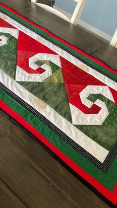 a quilted table runner with the letters gg on it, sitting on a wooden floor