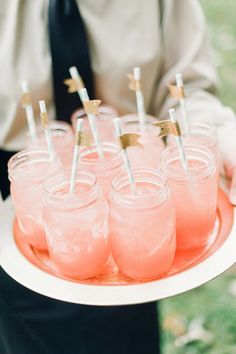 a man holding a tray filled with pink drinks and gold stars on top of them