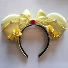 a yellow minnie mouse ears headband with flowers on it's side and a red bow at the top