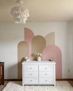 a white dresser sitting in front of a wall with pink and beige paint on it