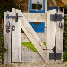 an old wooden gate with metal latches on the front and side, in front of a brick house