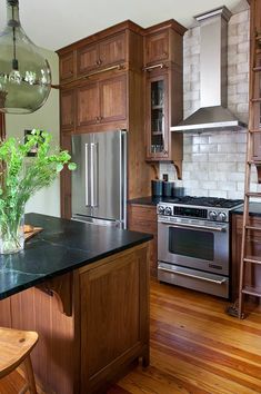 a kitchen with wooden cabinets and stainless steel appliances, along with a green plant in a vase on the island