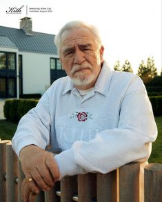 an old man leaning on a fence with his hand on the rail and looking at the camera