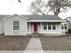 a gray house with a red door and two windows