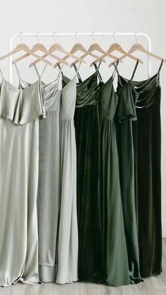 four dresses hanging on a clothes rack in front of a white wall and wooden floor