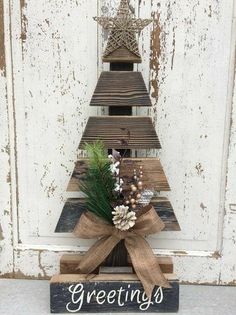 a wooden christmas tree sitting on top of a white door with the words greetings written below it