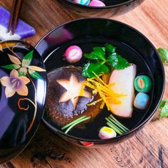 two black bowls filled with food on top of a wooden table next to chopsticks